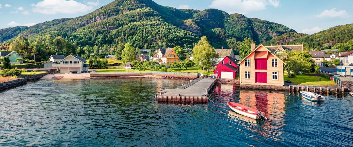 A lakeside village with houses, a dock, and a mountain in the background.