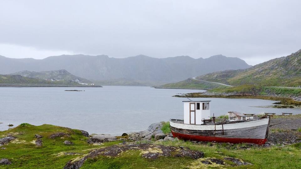 A boat on a rocky shore with mountains in the background.