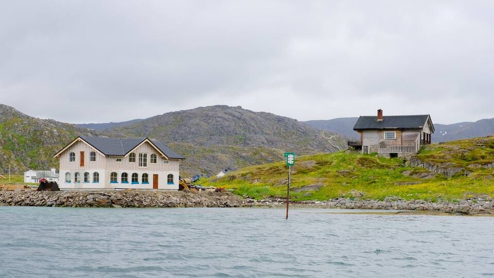 A coastal house with a rocky shoreline, a small dock, and a mountain backdrop.