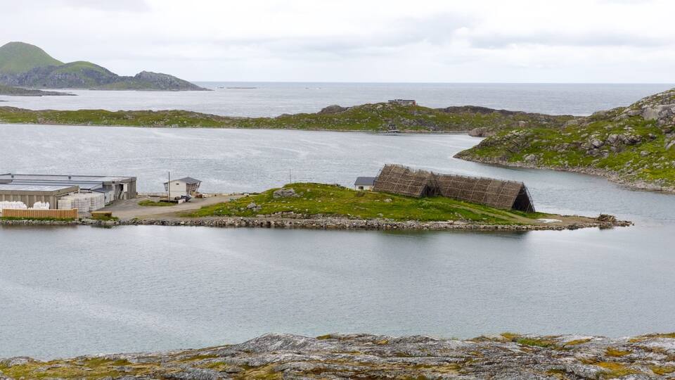 A coastal landscape with a large body of water, a small island with a traditional structure, and a modern building complex.