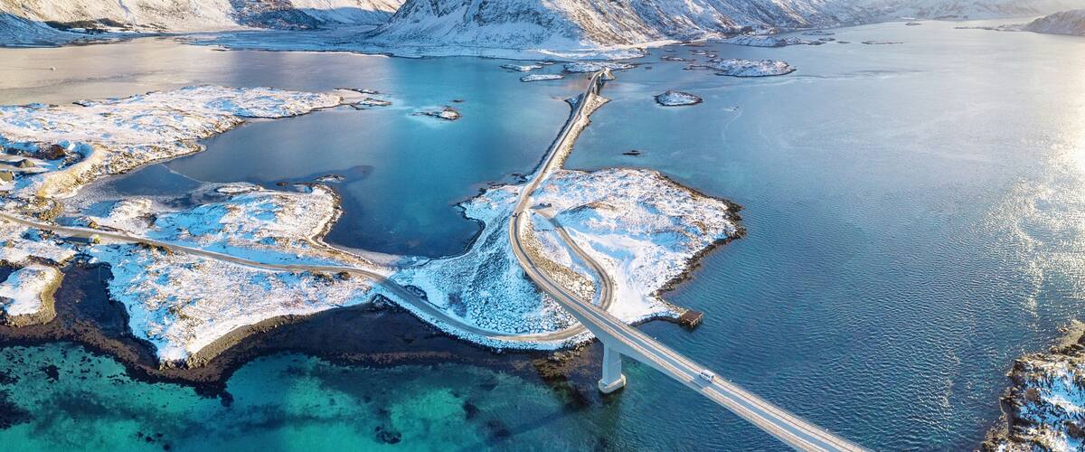 A snow-covered fjord with a bridge connecting islands, surrounded by mountains.