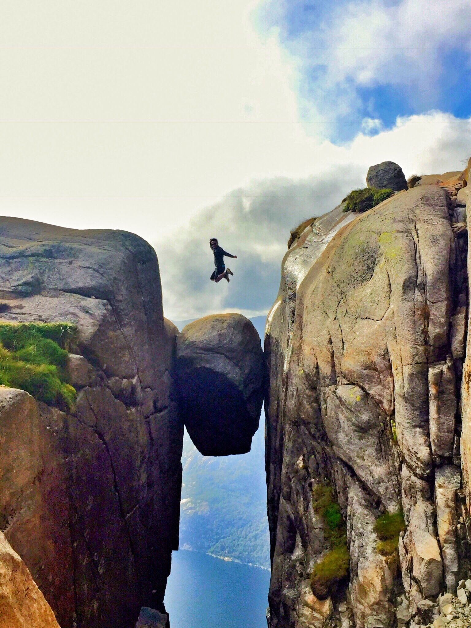 A person jumping between rock formations with a view of a body of water below.