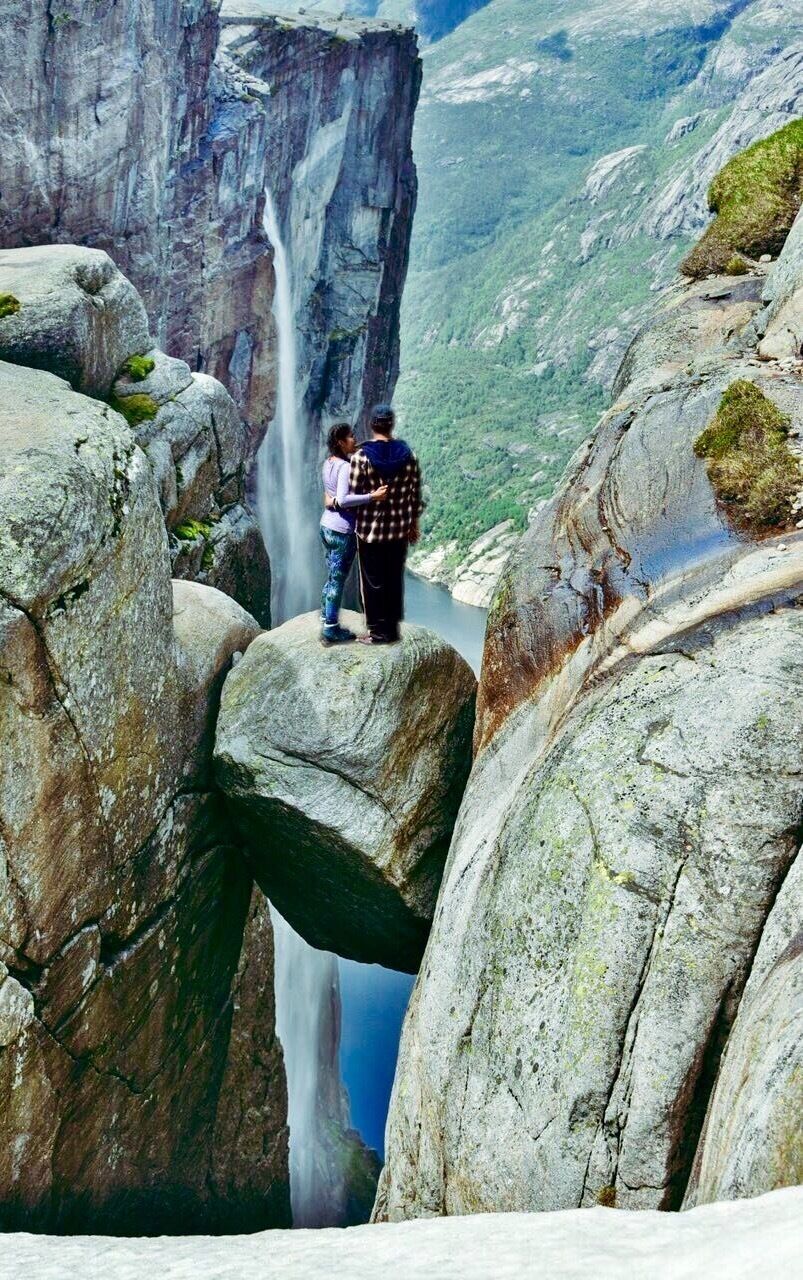 A waterfall cascading down a cliff, with two people standing on a rock ledge above it.