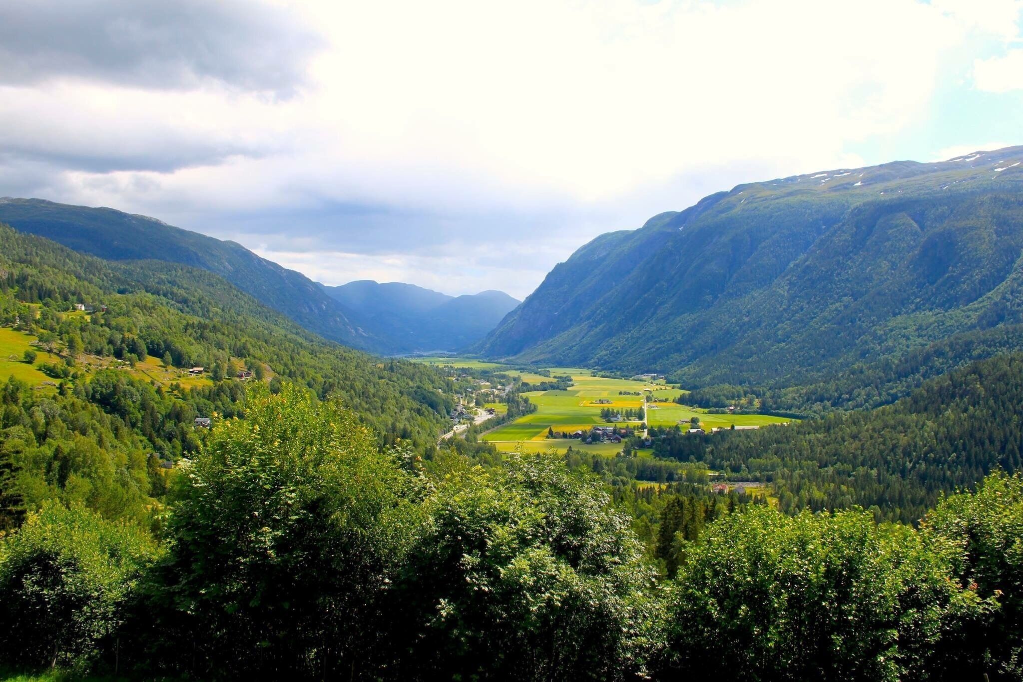 A valley with a river, surrounded by forested mountains and a few scattered buildings.