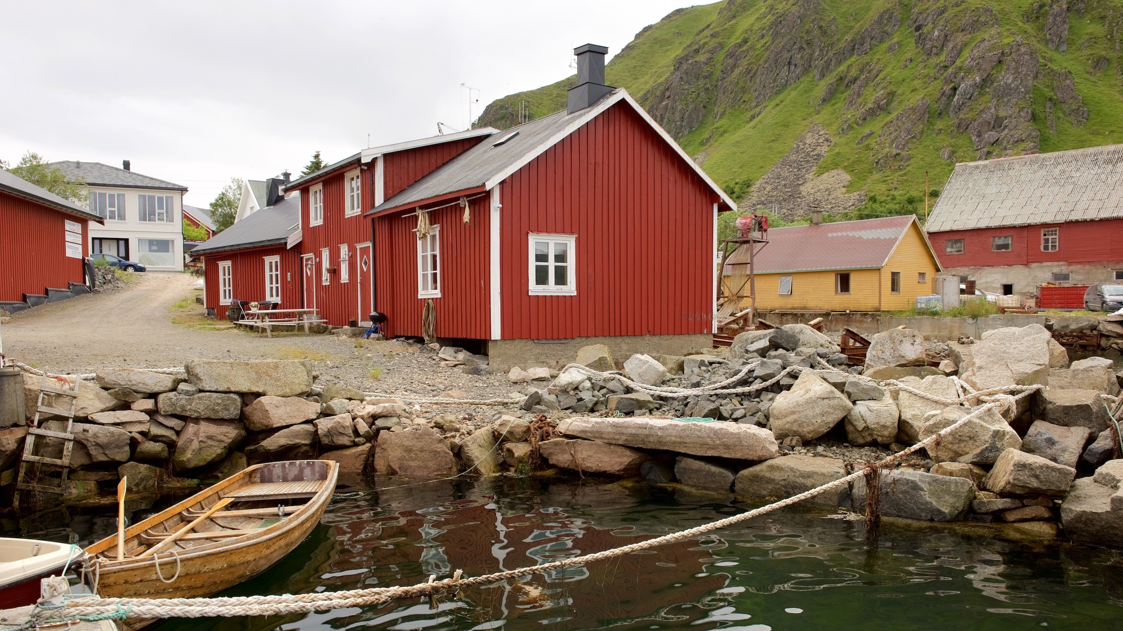 A coastal village with red wooden houses, a rocky shoreline, and a small wooden boat tied to the rocks.