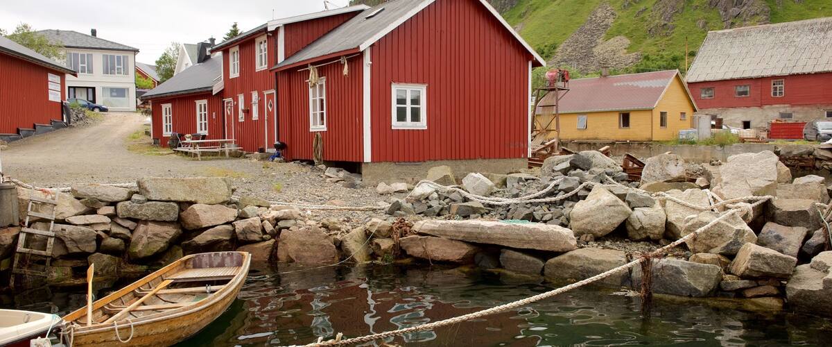 A coastal village with red wooden houses, a rocky shoreline, and a small wooden boat tied to the rocks.