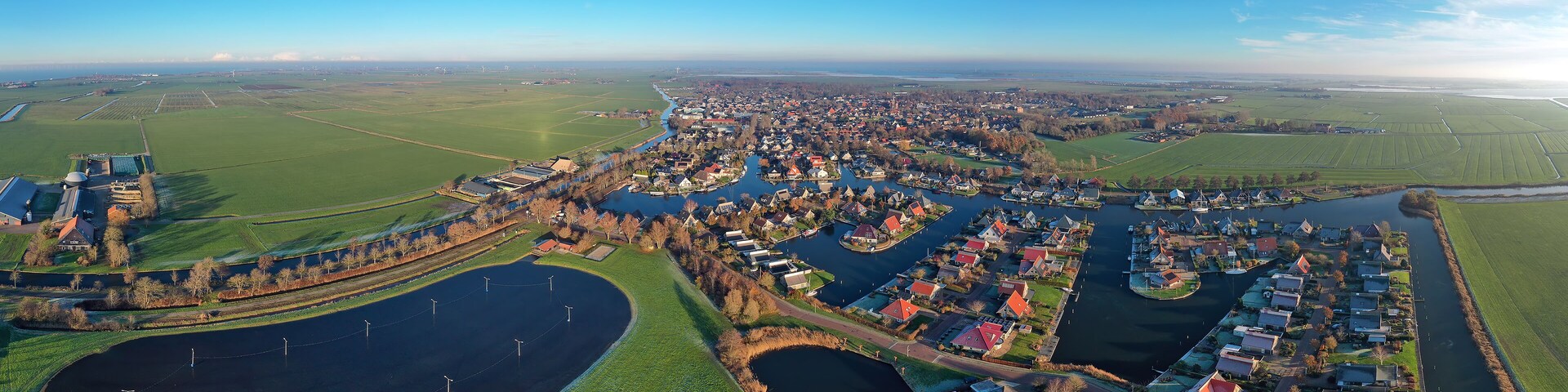 Vista aérea de un pueblo a orillas del río, con un extenso campo verde, un río sinuoso y varias casas a lo largo de la ribera.