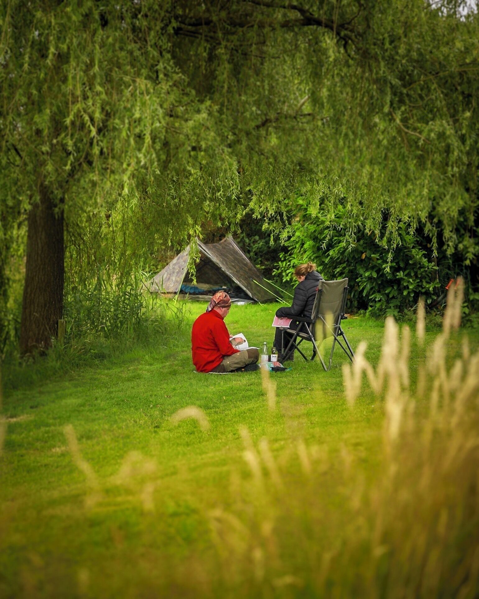 Two people sitting in a grassy field with a tent in the background.