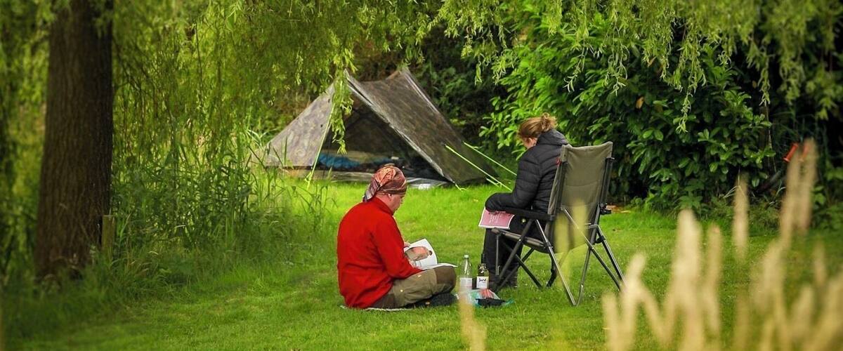 Two people sitting in a grassy field with a tent in the background.