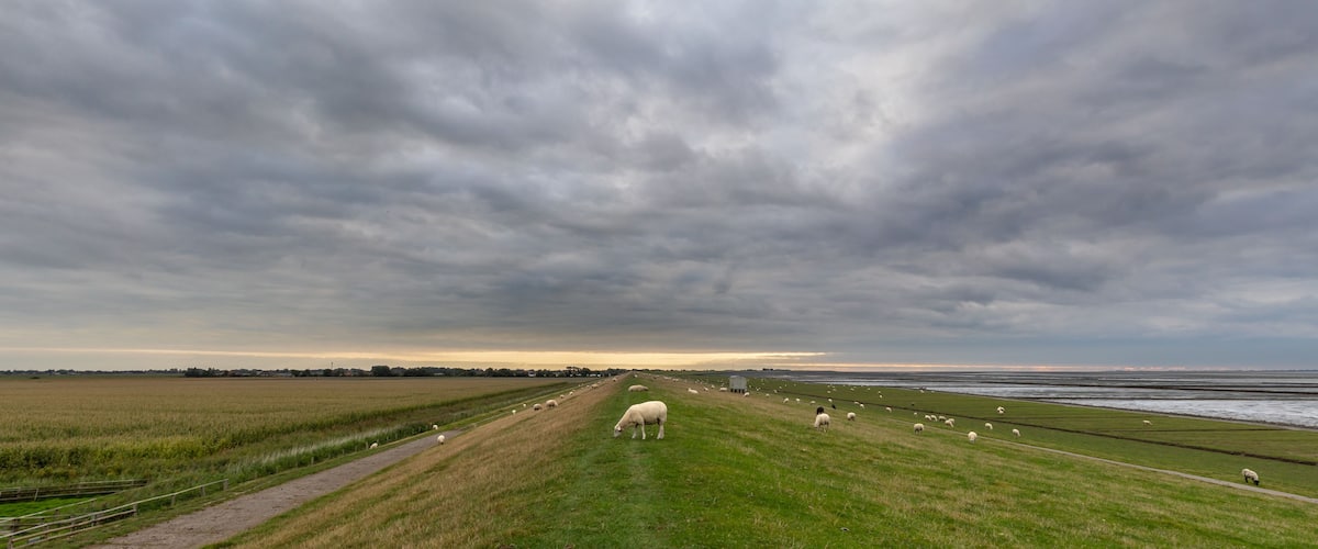 Overskyet himmel over et landligt landskab med marker og et vandareal.
