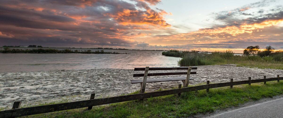 A sunset over a river with a wooden bench and a fence in the foreground.