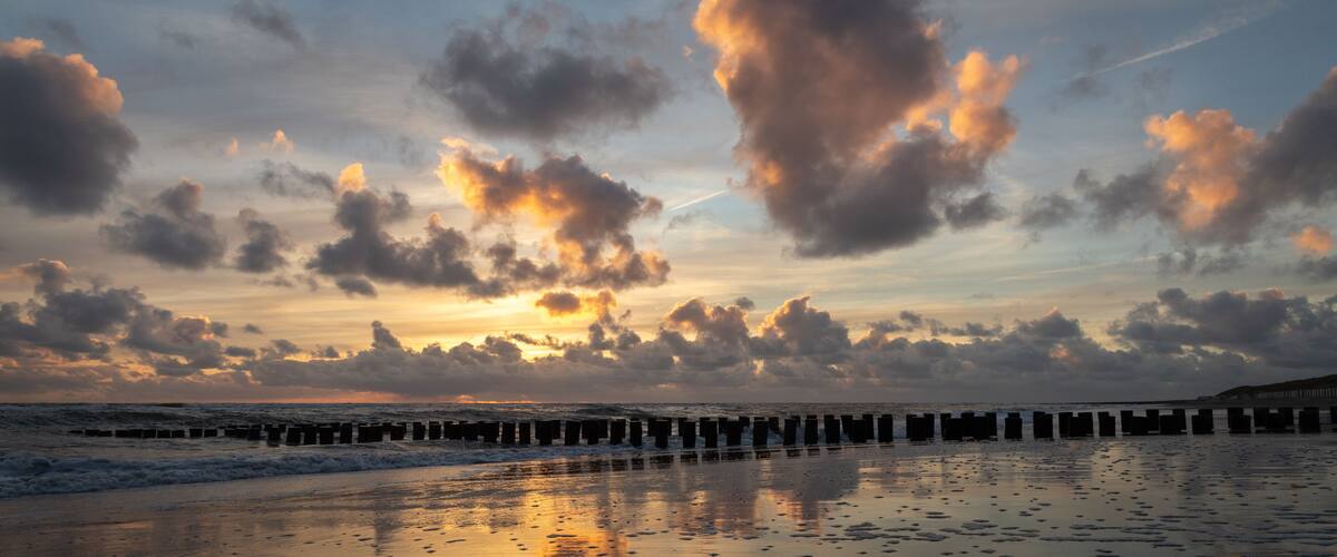 Sunset with colorful sky and clouds and wooden posts at Westenschouwen, Zeeland, the Netherlands