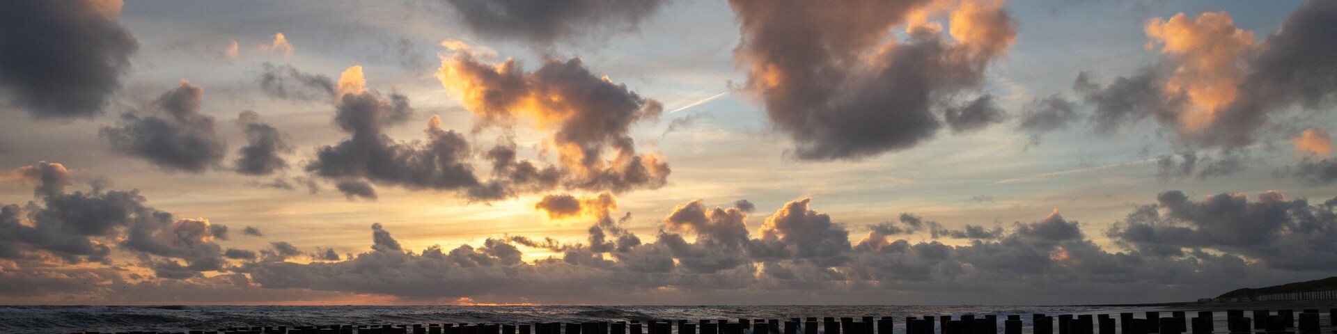 A beach with waves, a cloudy sky, and a sunset.