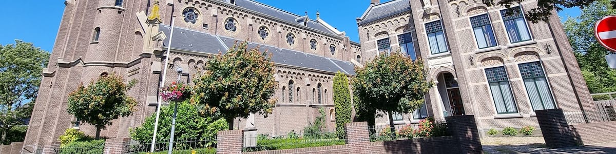 A historic church with a tall spire, brick architecture, and a large tree in the foreground.