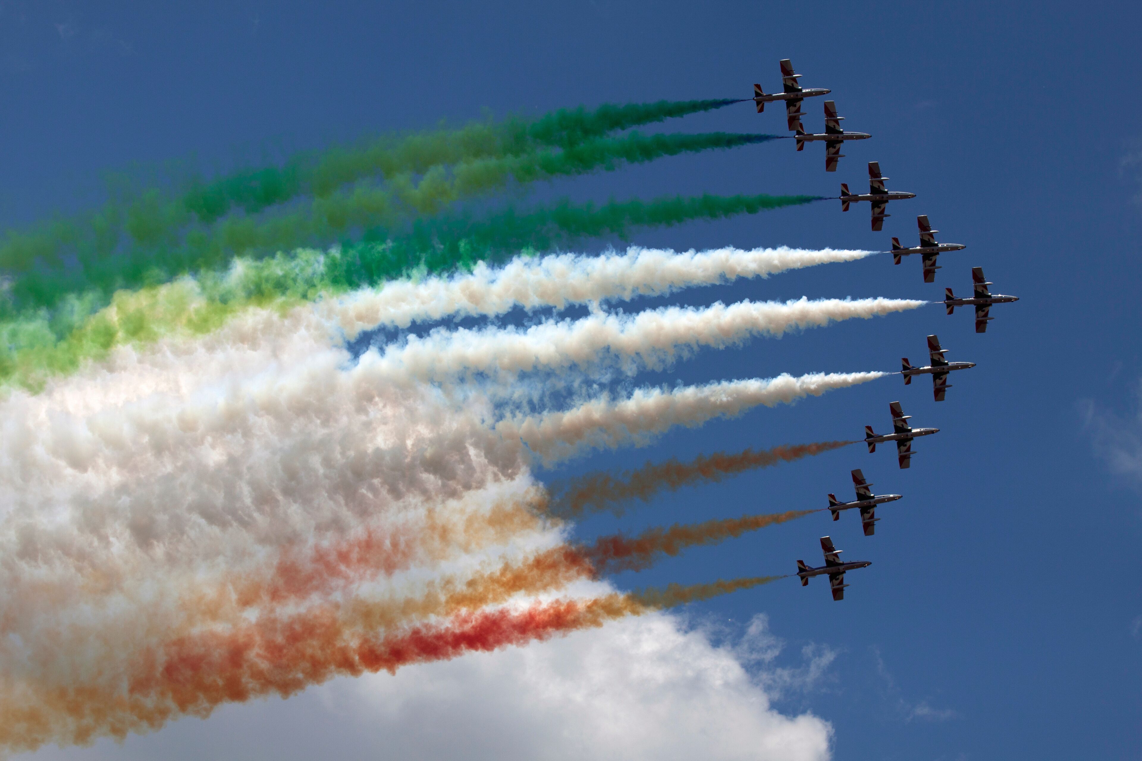 A formation of jets flying in a clear sky with colored smoke trails.