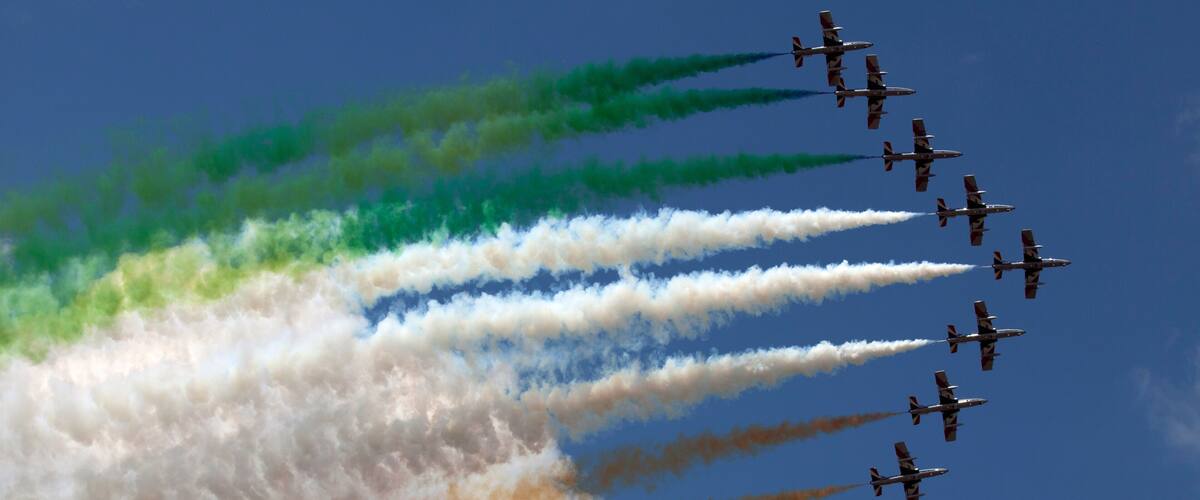 A formation of jets flying in a clear sky with colored smoke trails.