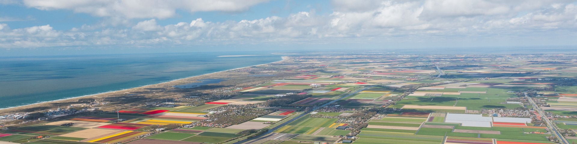 An aerial view of a coastal landscape with farmland, a coastline, and a distant city.