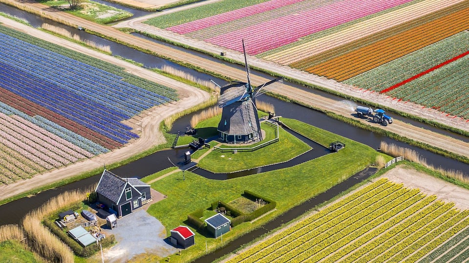 An aerial view of a windmill surrounded by agricultural fields, a small building, and a river.