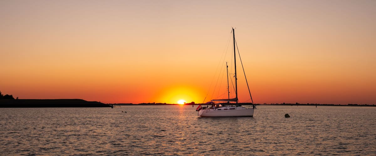 A sailboat on calm waters at sunset with a clear sky.