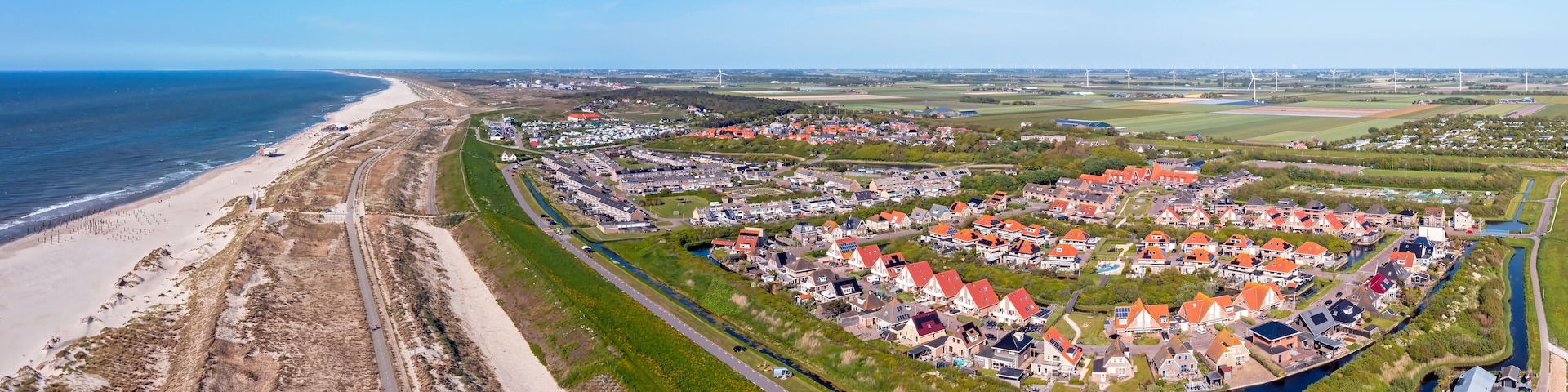 Eine Luftaufnahme einer Küstenstadt mit Strand, Häusern und Windkraftanlagen.
