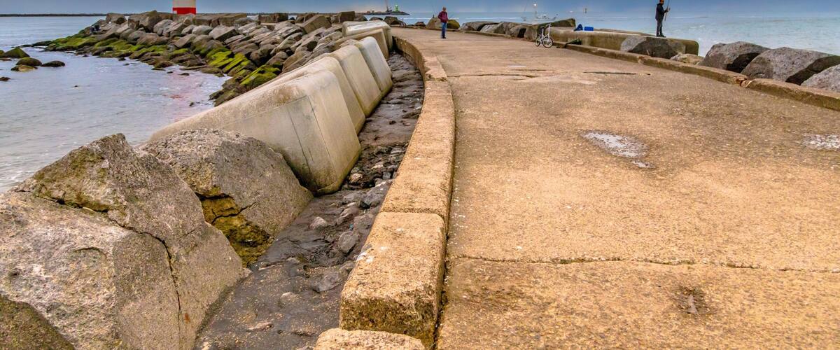 A coastal walkway with a lighthouse, rocky shore, and fishing activity.