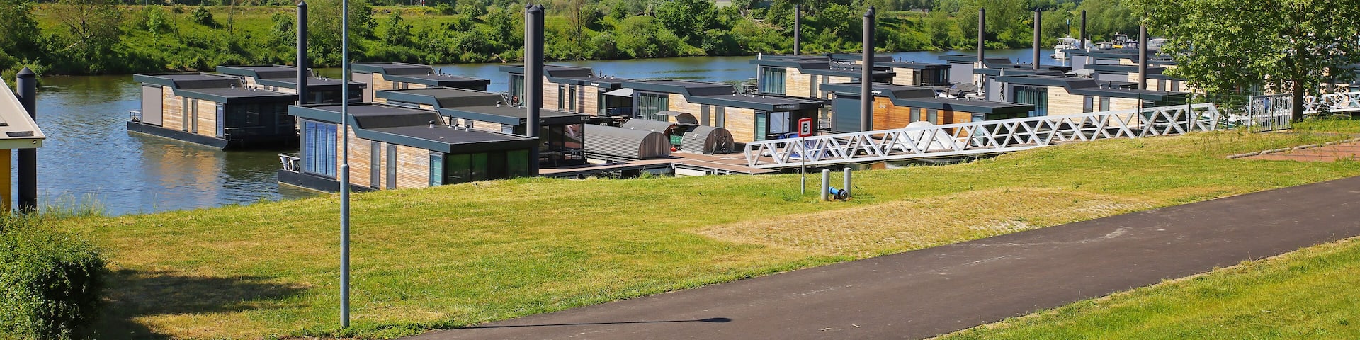 Ohe en Laak, Netherlands - May 9. 2022: View on cycle path along vacation houseboats on river Maas, green countryside landscape, blue spring time sky