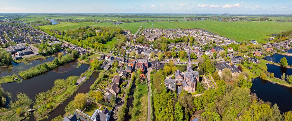 An aerial view of a town with a river, green fields, and a church.