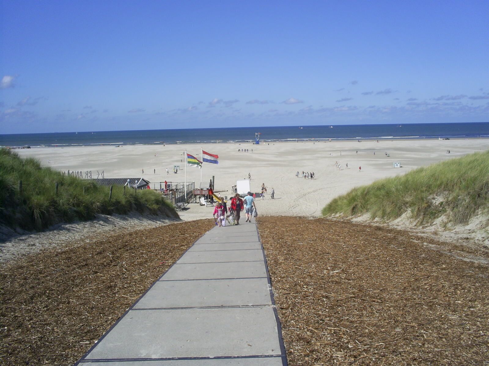 A beach with a concrete walkway leading to the shore, a flag, and the ocean in the background.