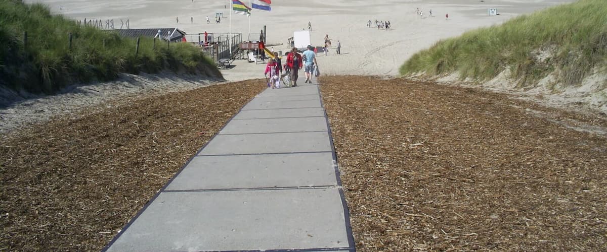 A beach with a concrete walkway leading to the shore, a flag, and the ocean in the background.