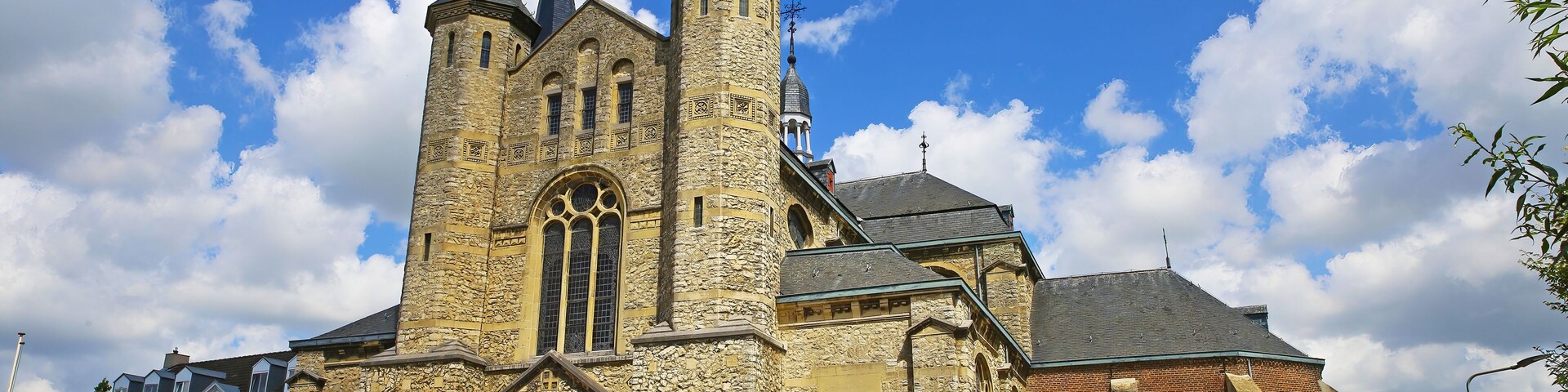 Una iglesia histórica con una alta torre central, puertas rojas y fachada de piedra.
