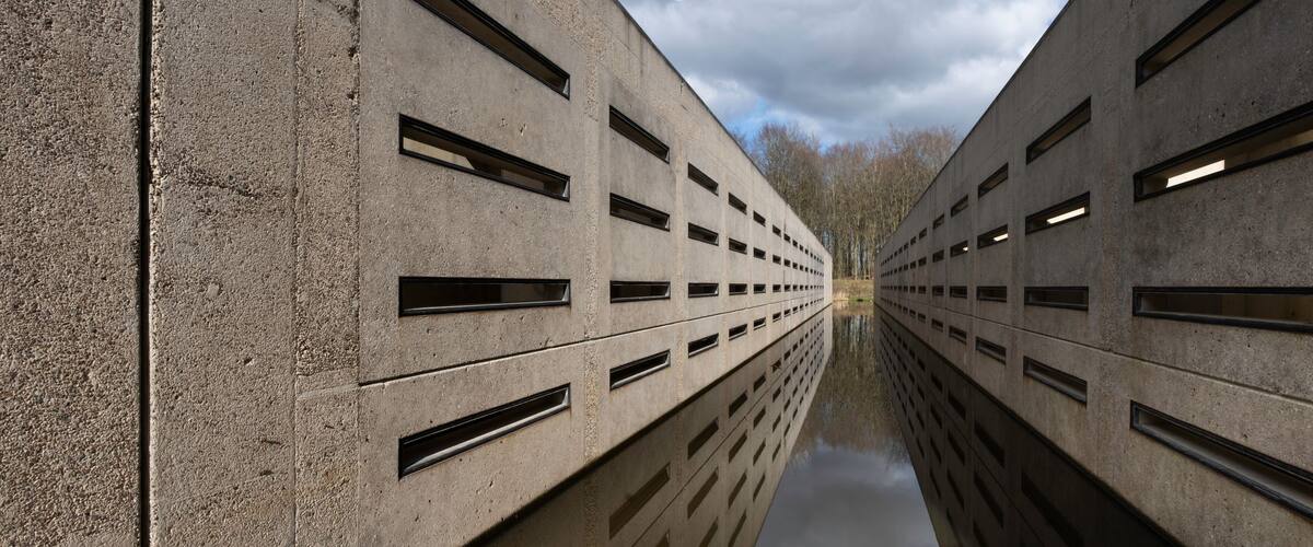 A symmetrical concrete structure with multiple rectangular windows and a reflective water surface.