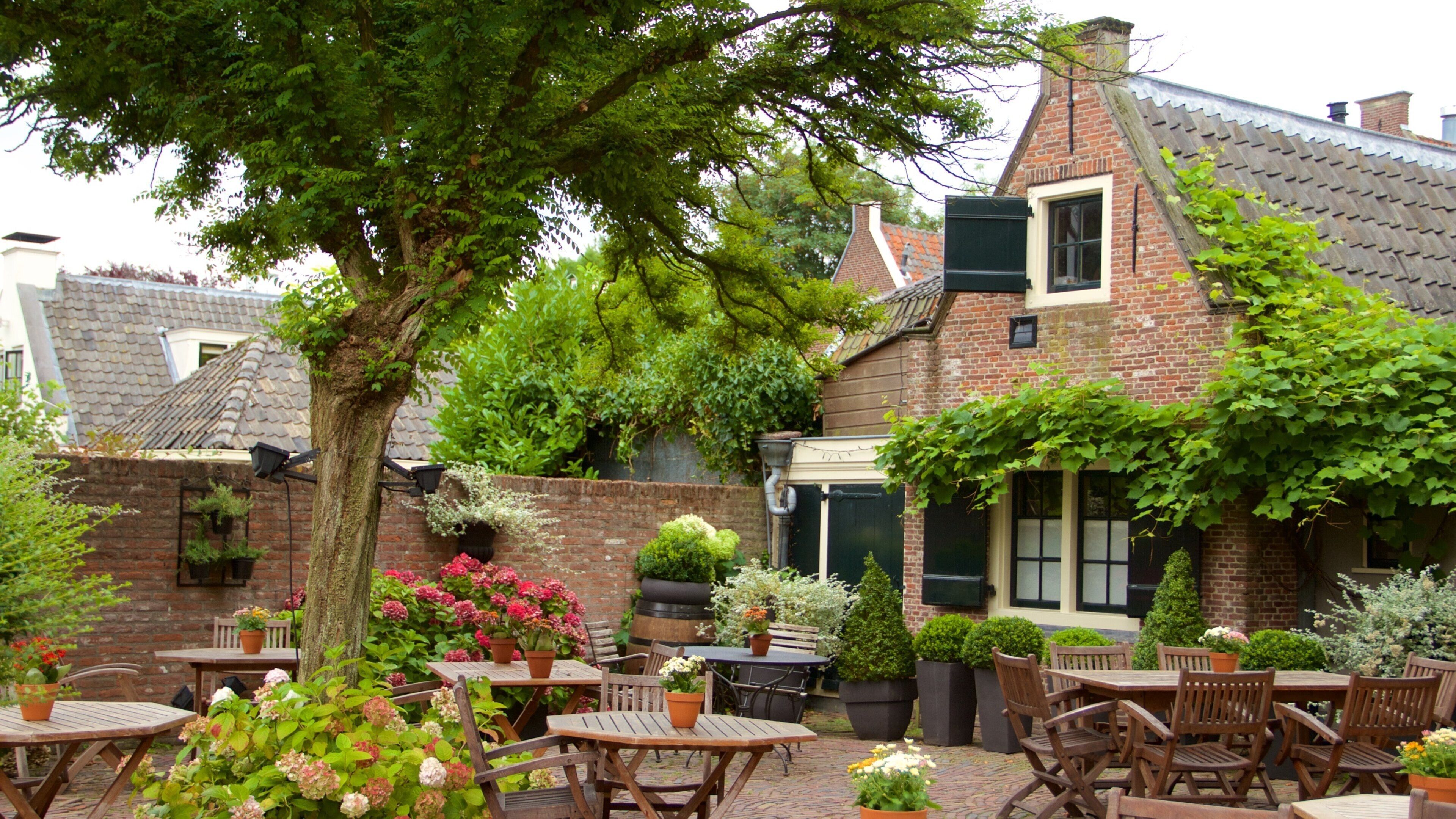 A brick building with a sloped roof, surrounded by lush greenery and outdoor seating.