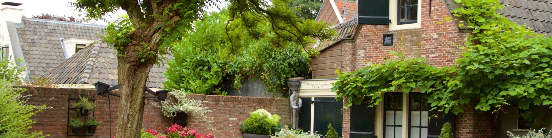 A brick building with a sloped roof, surrounded by lush greenery and outdoor seating.