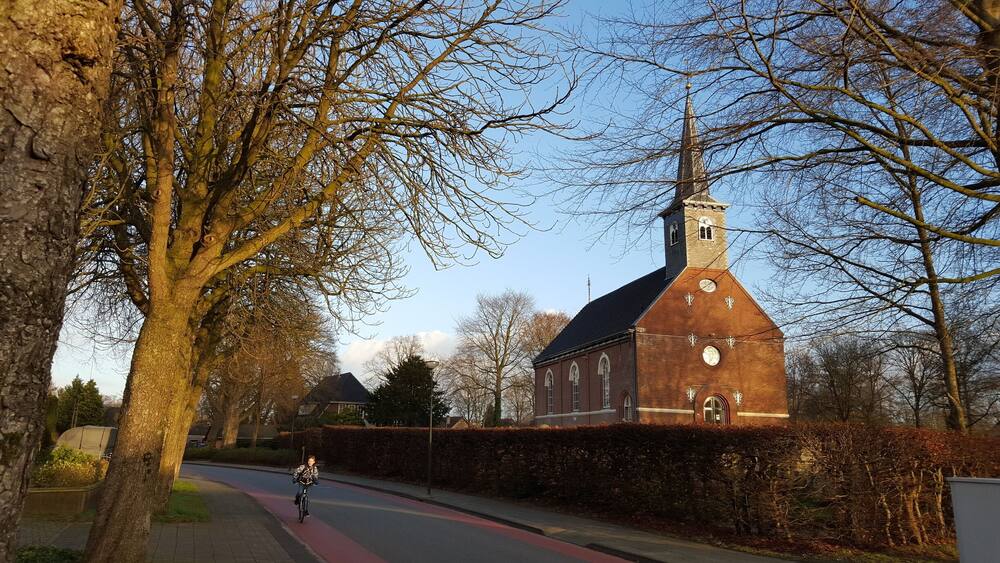A cyclist on a red bike lane beside a church with a clock tower.