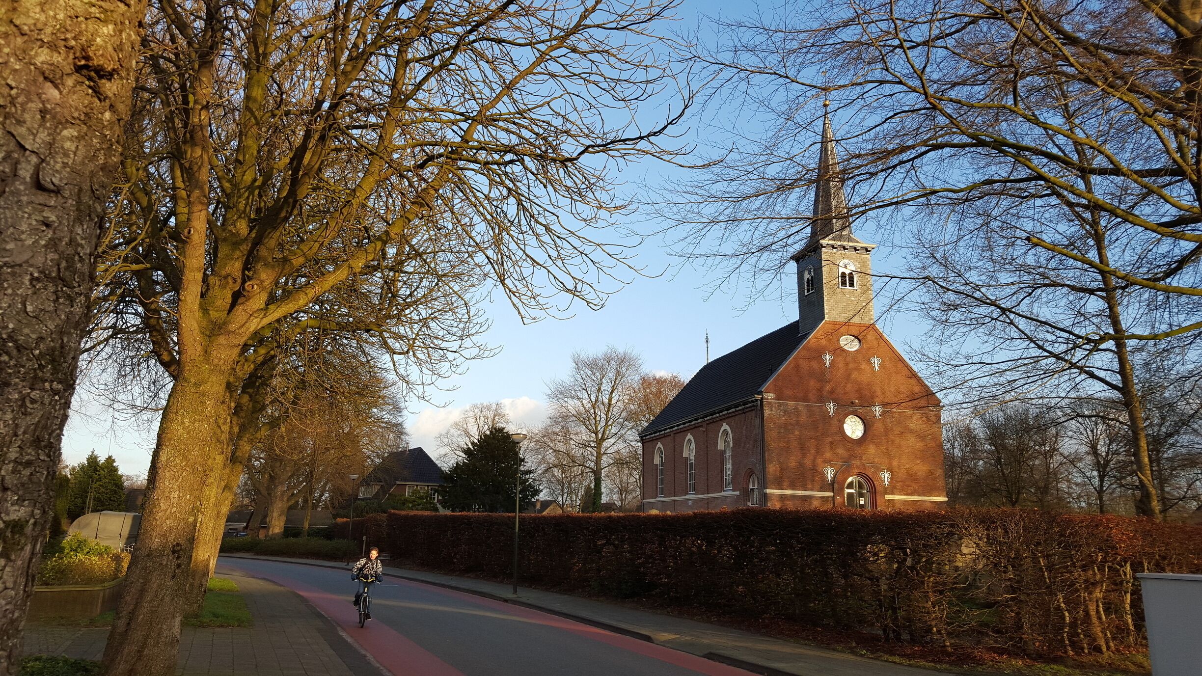 A cyclist on a red bike lane beside a church with a clock tower.