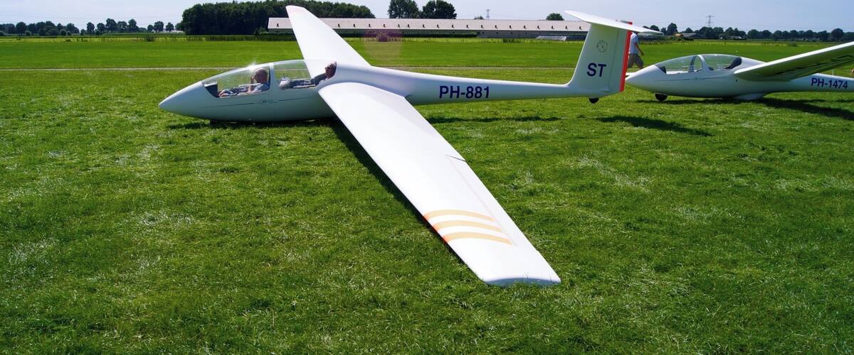 Two gliders on a grassy field with a building in the background.