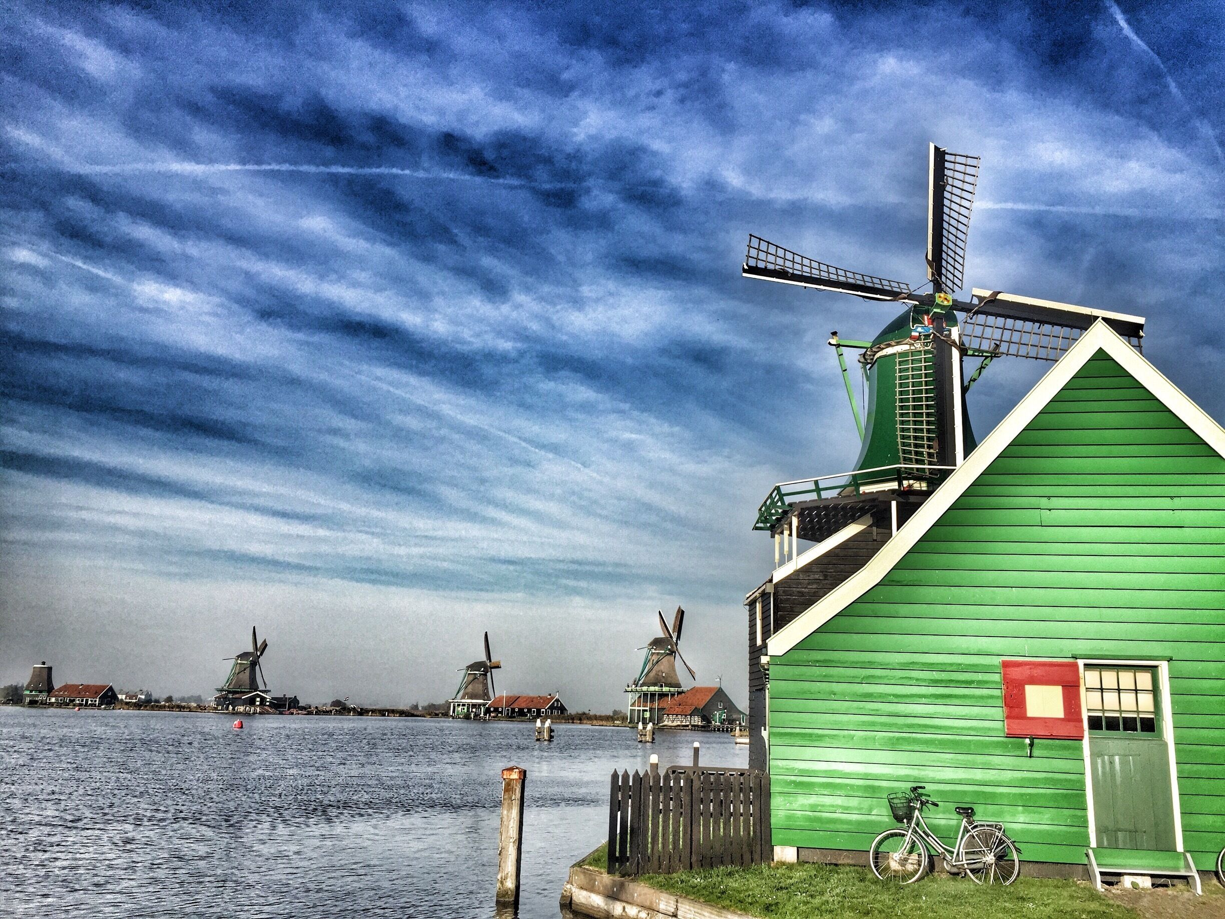 A green windmill and a green building by a body of water.