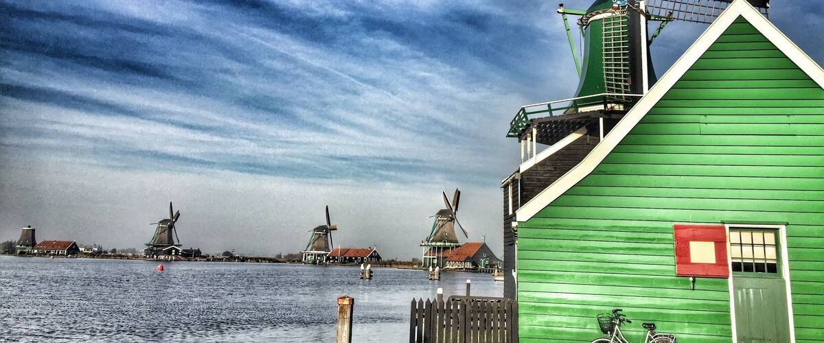 A green windmill and a green building by a body of water.