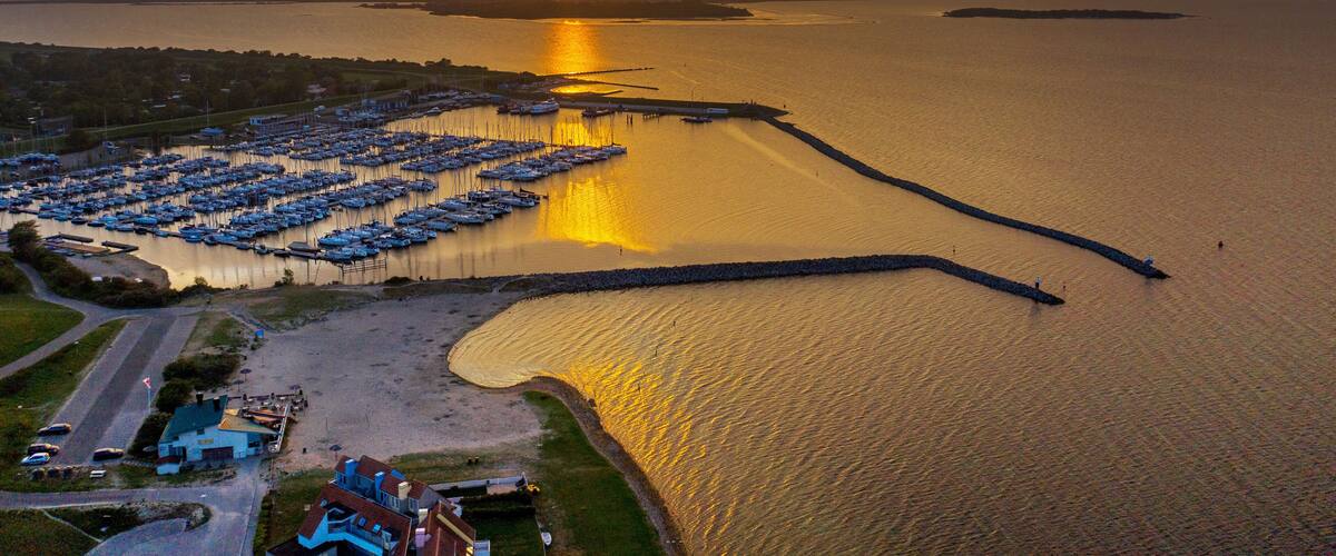 A marina with boats, a pier, and a sunset over a calm body of water.