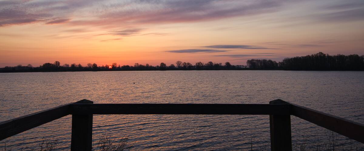 A sunset over a calm lake with a wooden dock in the foreground.