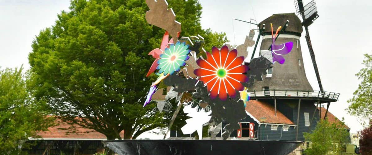 A windmill, a sculpture with colorful flowers, and a tree in a park.