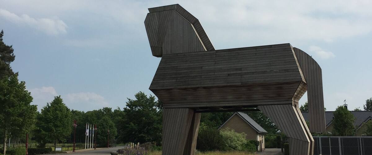 A large wooden sculpture of a horse in a grassy area.