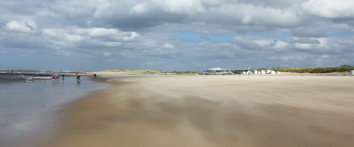 A wide sandy beach with a few people and a white building in the distance.