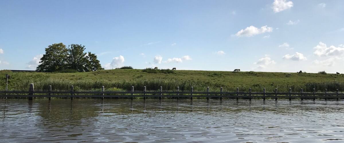 A calm water body with a wooden fence and a grassy hill in the background.