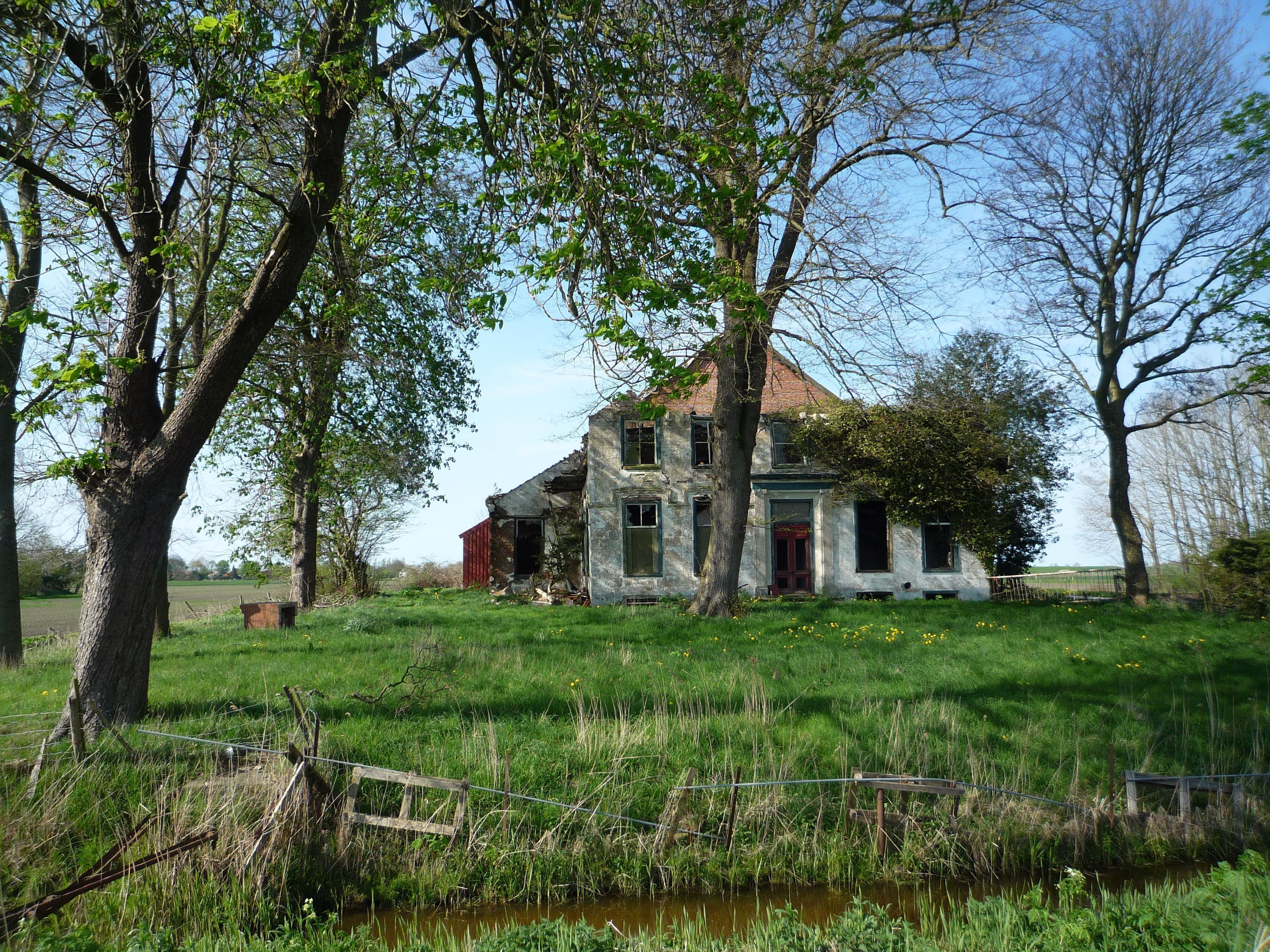 An old, dilapidated house surrounded by lush greenery and a small pond.