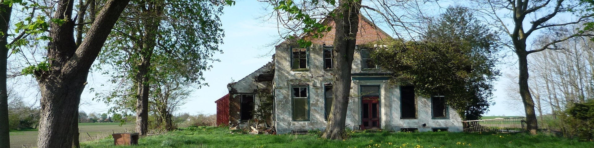 An old, dilapidated house surrounded by lush greenery and a small pond.