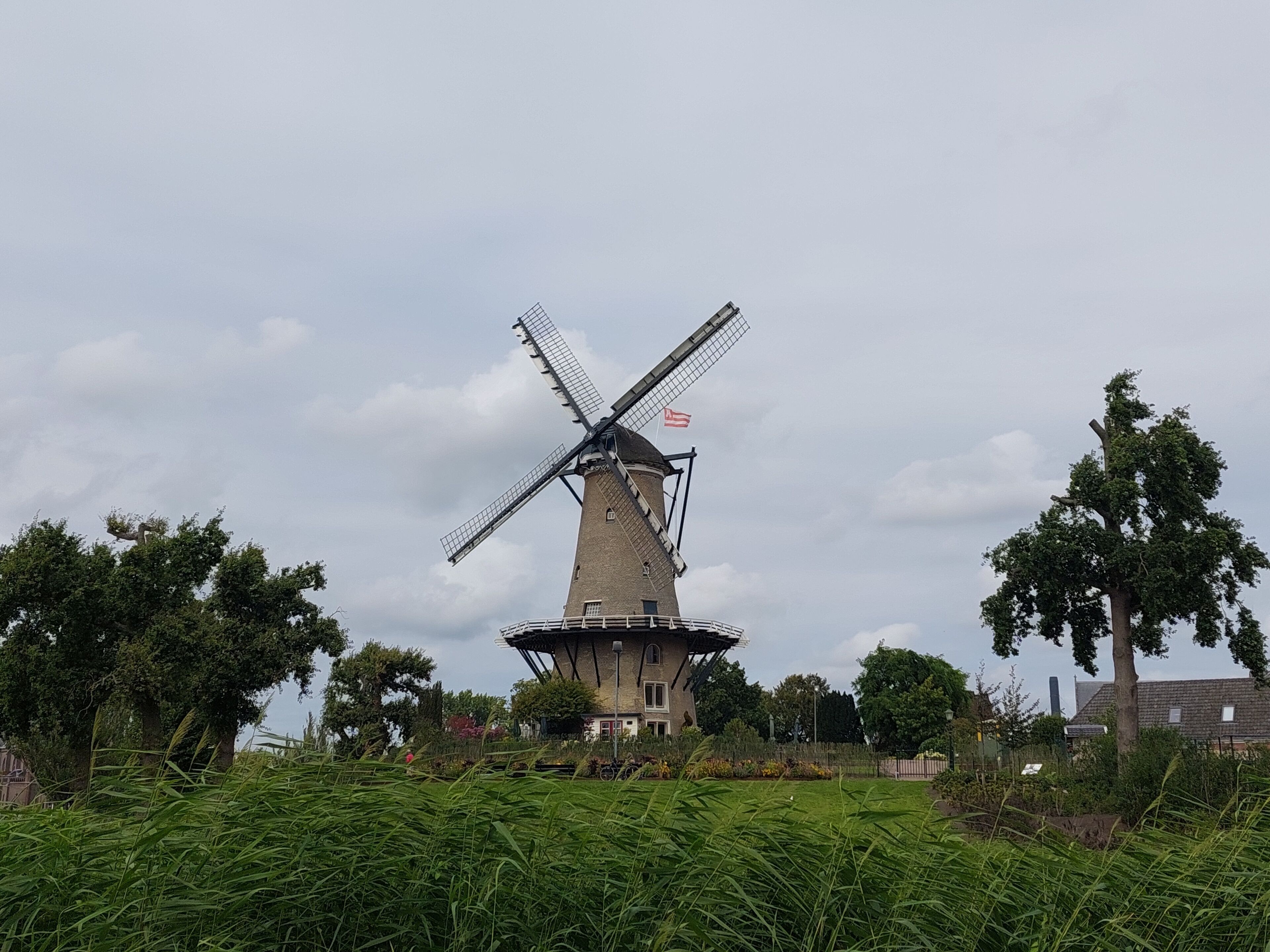 A traditional windmill with a flag, surrounded by lush greenery and trees.