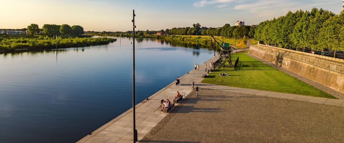 A river with a paved walkway, green grass, and trees along the banks.