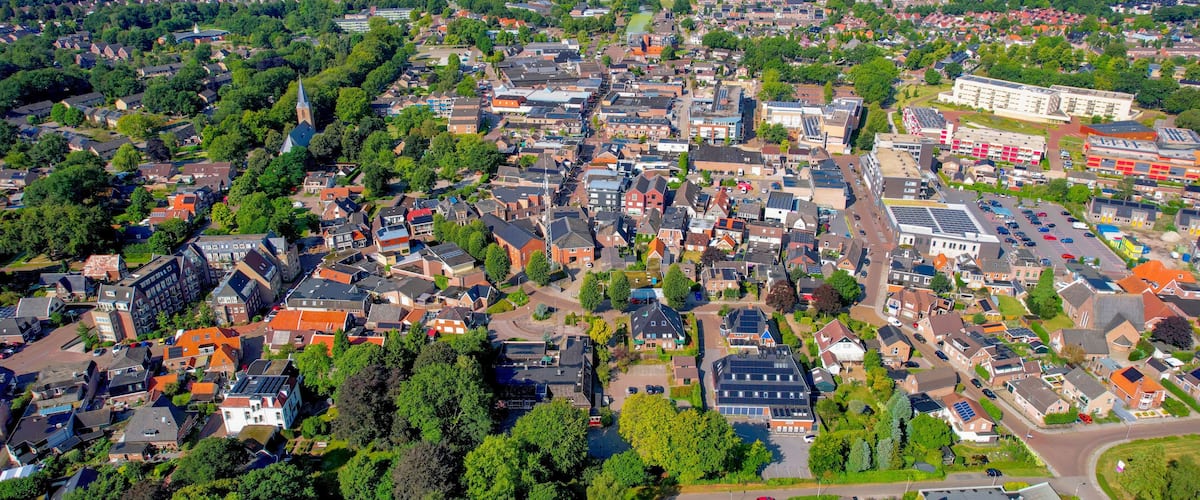 An aerial view of a town with dense housing, green spaces, and a large industrial building.