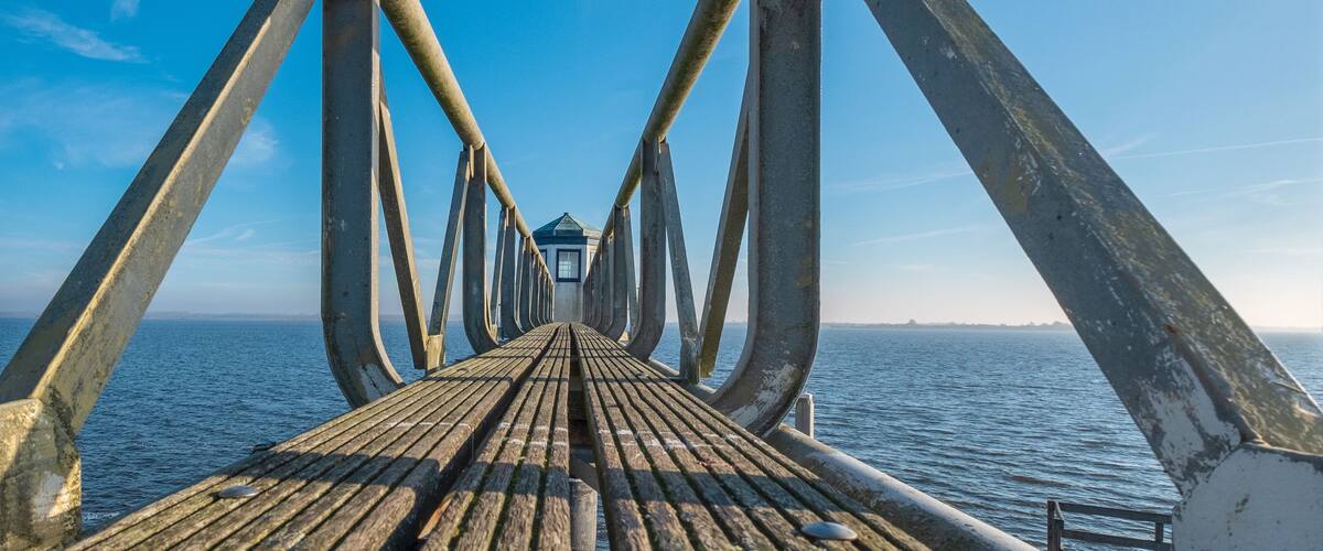 A wooden pier extending into the water with metal railings and a small building at the end.